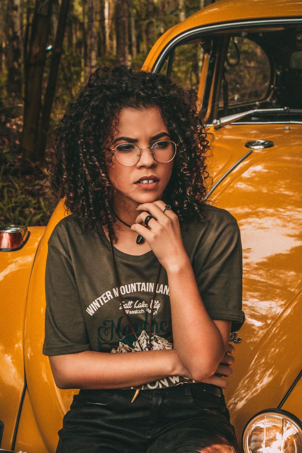 Free Image of Woman Wearing Glasses Sitting in Front of Yellow Car 