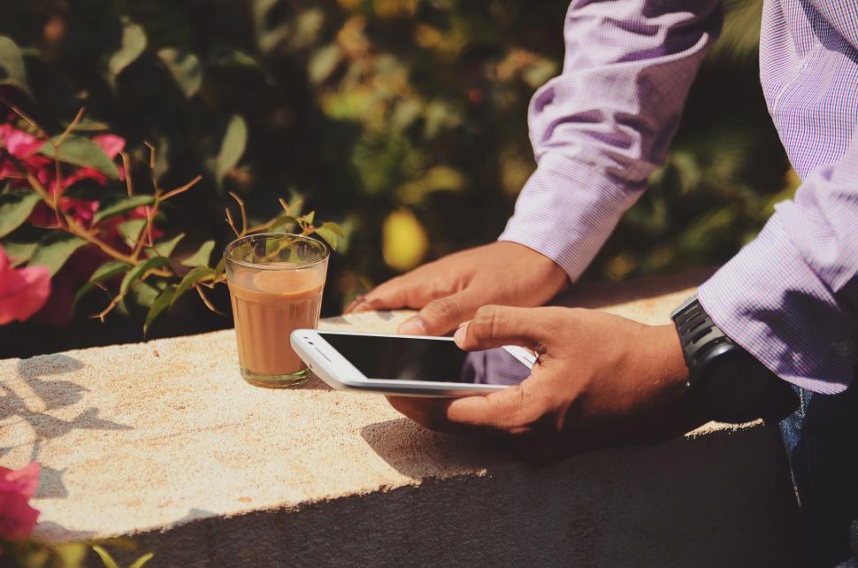 Free Image of Man Holding Smart Phone Next to Cup of Coffee 