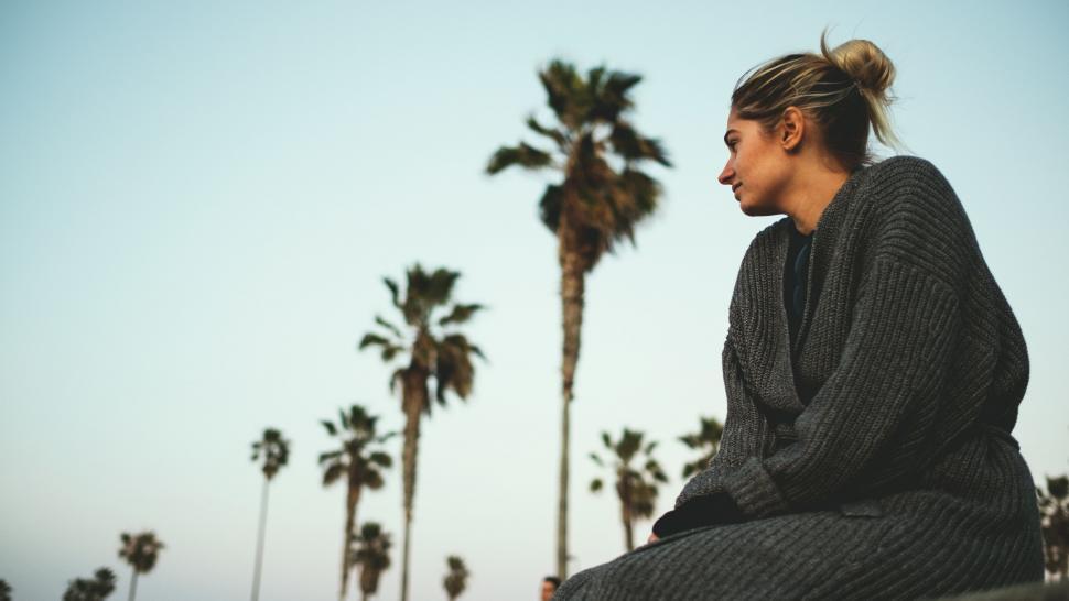 Free Image of Woman Sitting on Ledge With Palm Trees in Background 