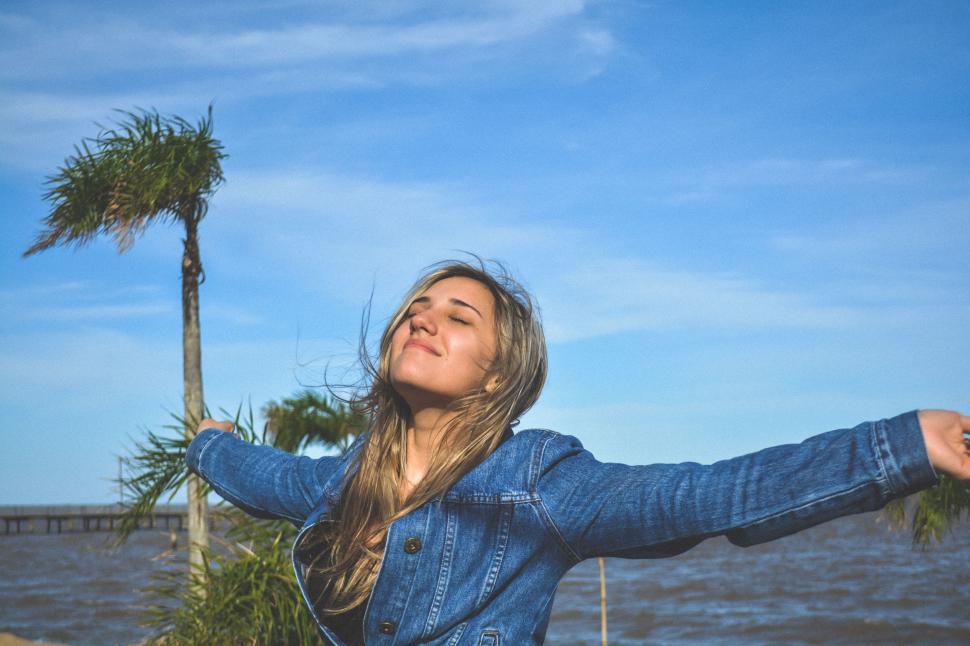 Free Image of Woman Standing Next to Palm Tree by Ocean 