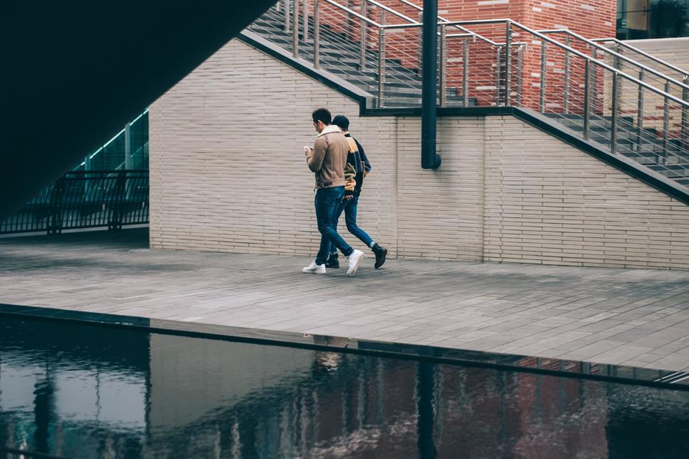 Free Image of Two Men Walking Down Sidewalk Next to Building 