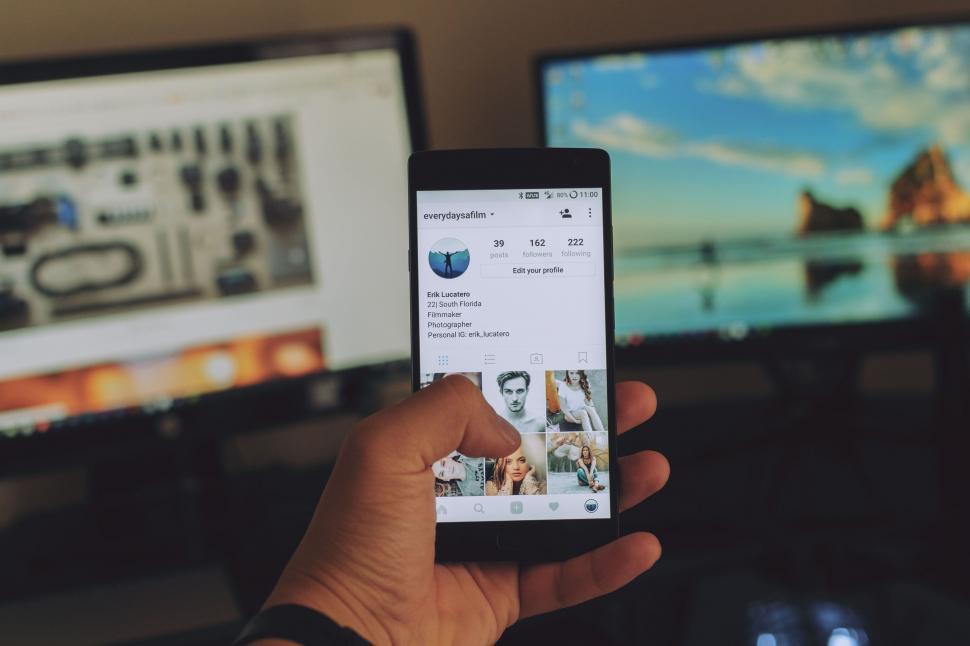 Free Image of Person Holding Cell Phone in Front of Two Televisions 
