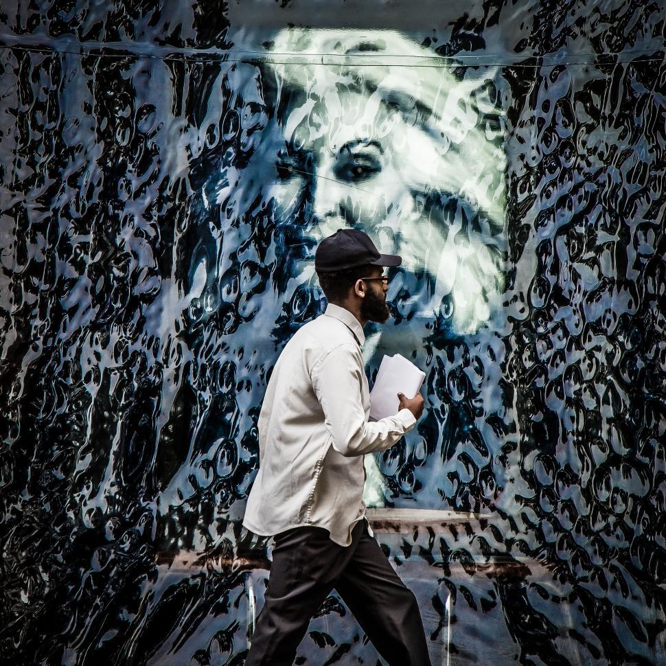 Free Image of Man Walking Past Painting of Woman 