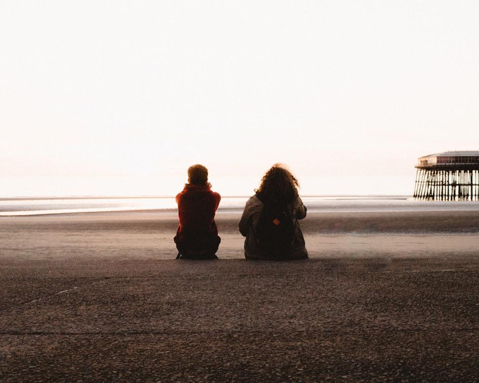 Free Image of Two People Sitting on Sandy Beach 