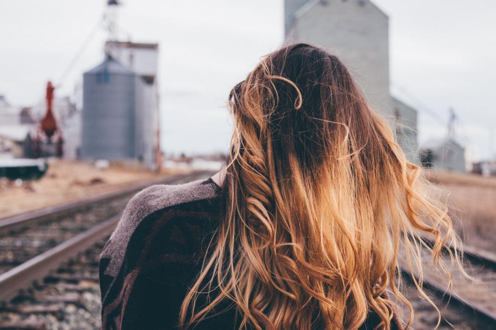 Free Image of Woman Standing on Train Tracks With Hair Blowing in Wind 