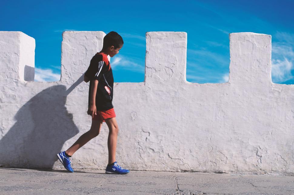 Free Image of Man Walking Down Street Next to White Wall 