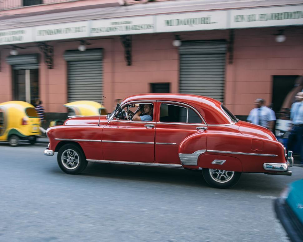 Free Image of Red Car Driving Down Street Next to Tall Buildings 