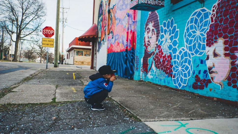 Free Image of Young Boy Squatting in Front of Graffiti Wall 