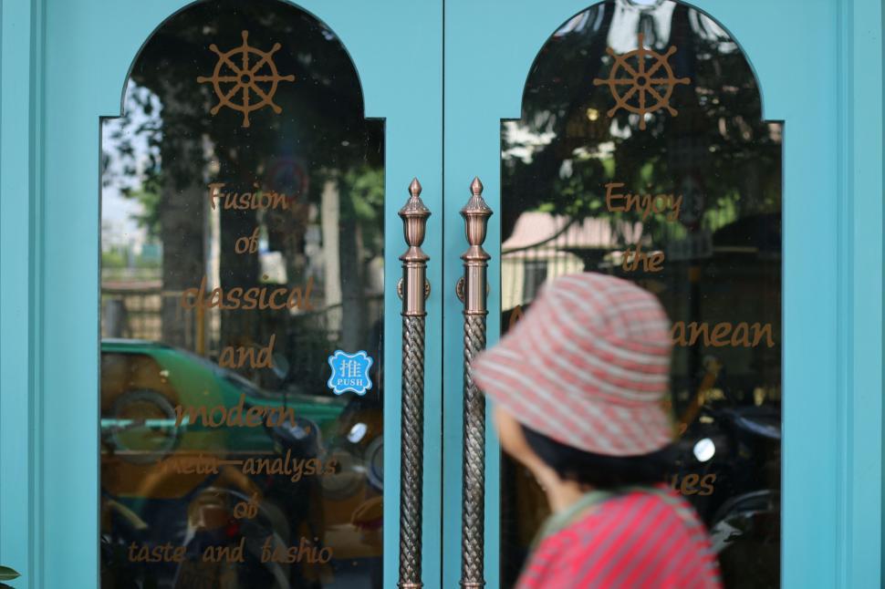 Free Image of Woman in Pink and White Hat Walking Past Blue Door 