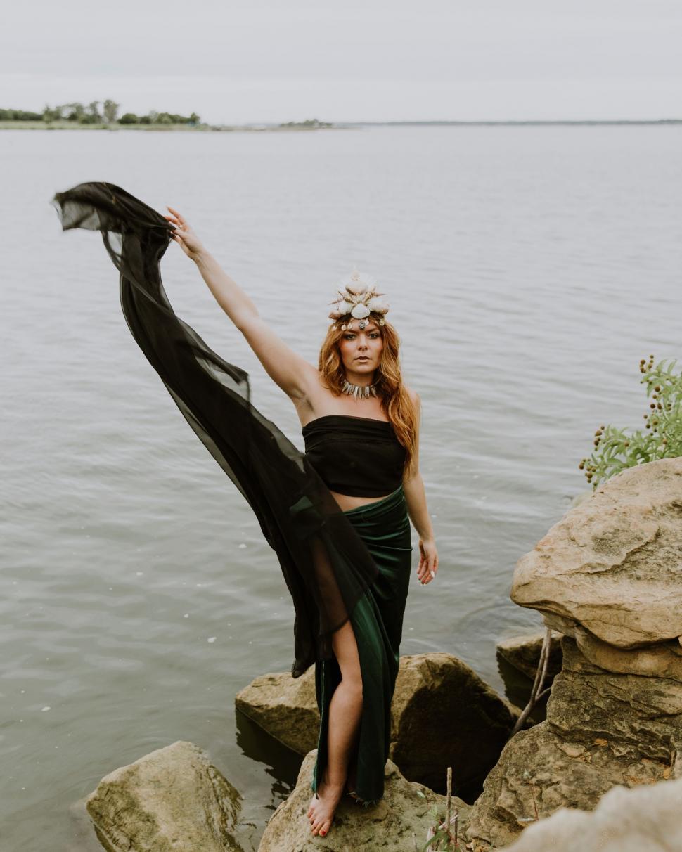 Free Image of Woman in Black Dress Standing on Rocks by Water 