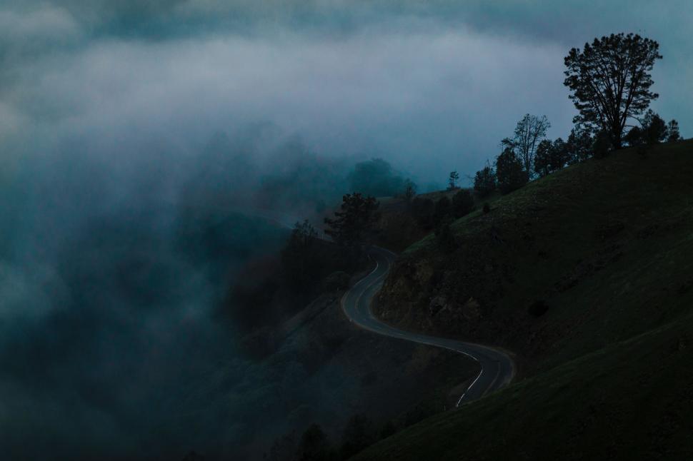 Free Image of Dark Sky With Clouds and Trees on a Hill 