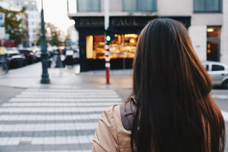 Free Image of Woman Walking Down a Street Next to a Tall Building 