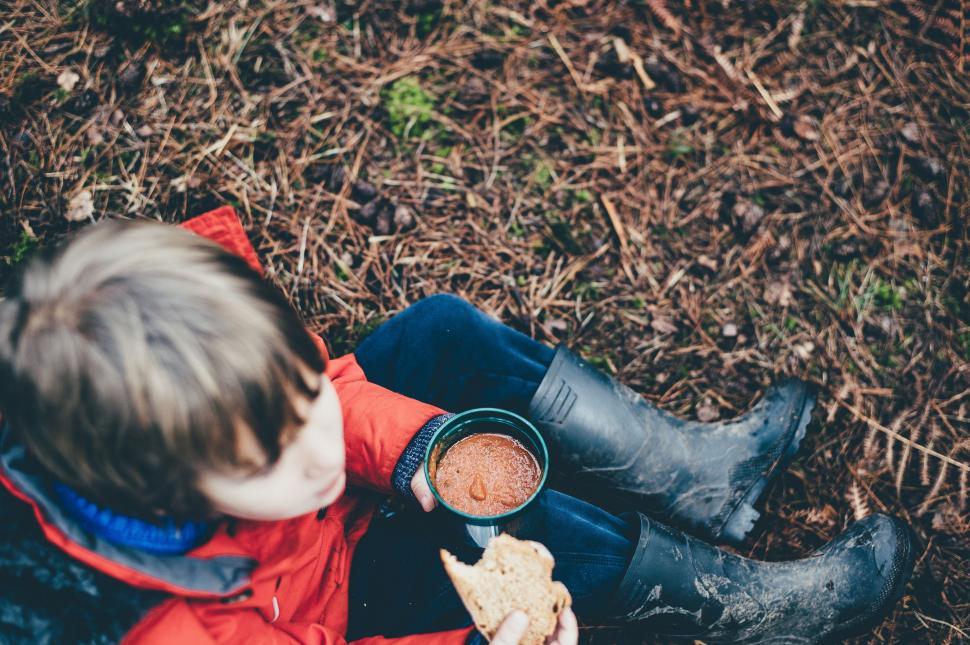 Free Image of Young Boy Sitting on the Ground Eating a Hot Dog 