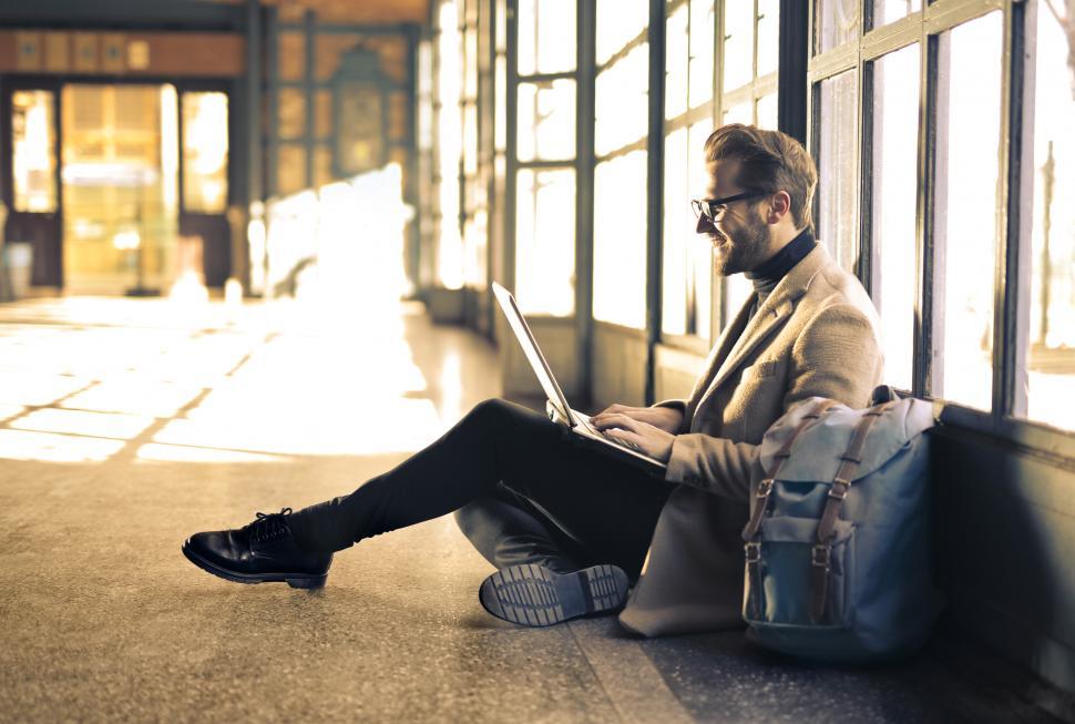 Free Image of Young Adult Man sitting and using a laptop inside an empty room 