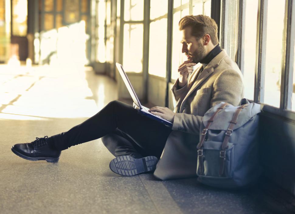 Free Image of Young Adult Man sitting and using a laptop inside an empty room 