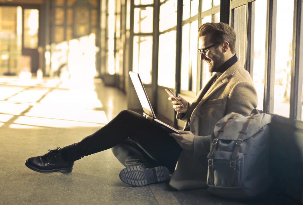 Free Image of Young Adult Man using a laptop and smiling as he looks on his ce 