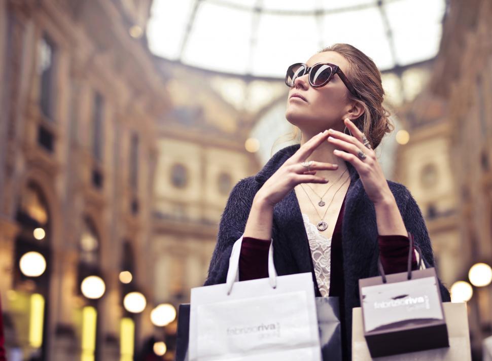 A young blond woman with elegant hair bun posing with shopping b