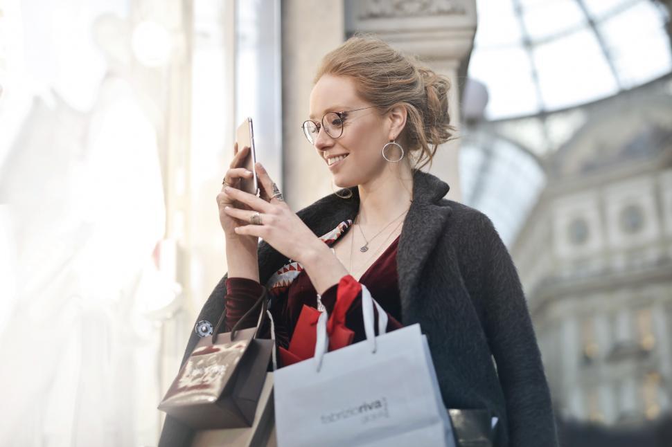 Free Image of A young blond woman looks at her mobile phone while holding shop 