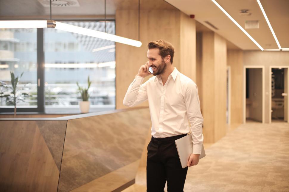 Free Image of A young caucasian man using his mobile phone and holding a lapto 