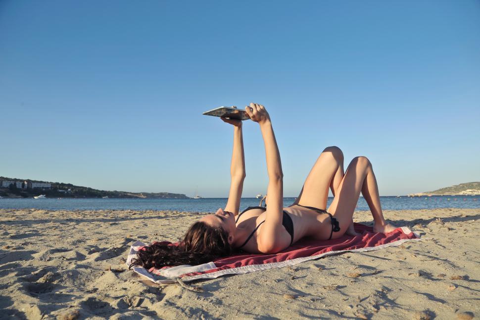 Woman in black bikini using an ipad while lying on beach sand