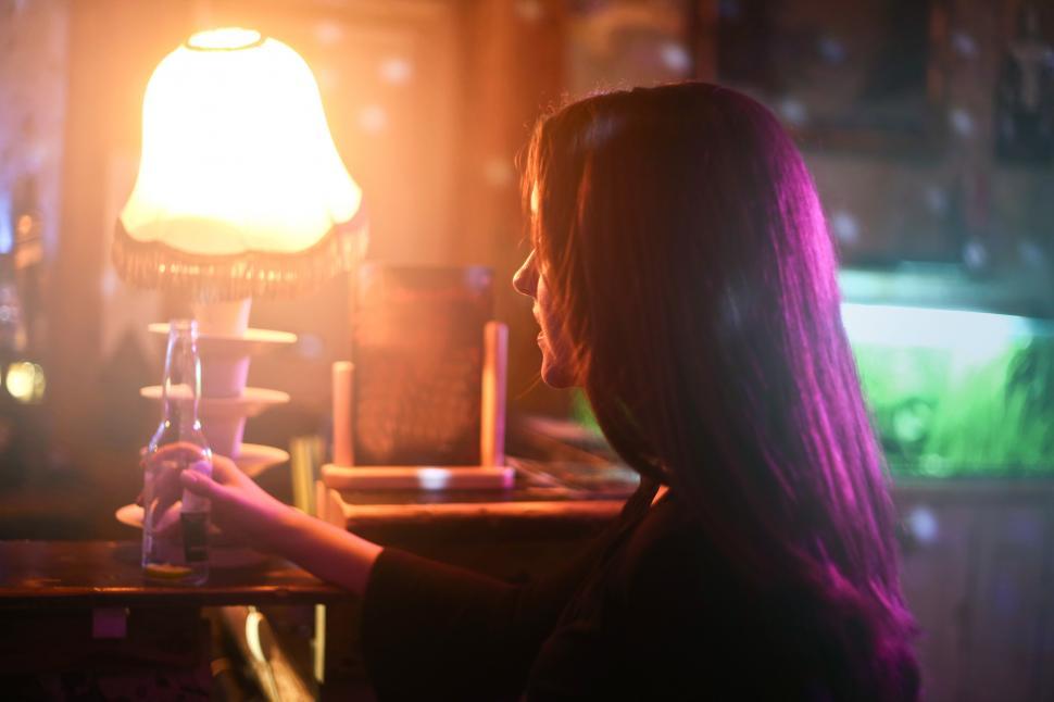 Free Image of A young brunette woman holding a beer pint bottle in a bar 
