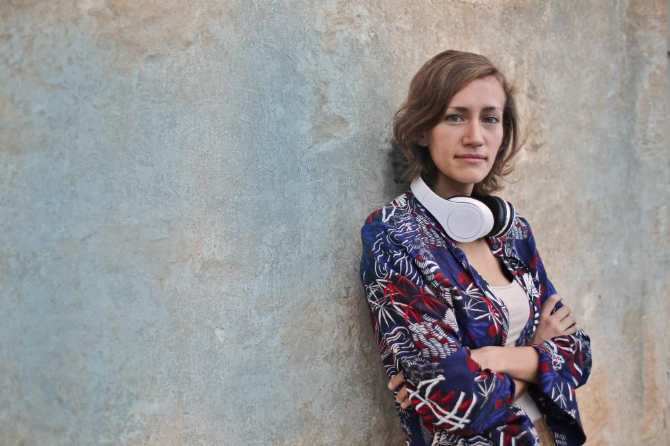 Free Image of A young blonde woman standing against a wall with a headset arou 