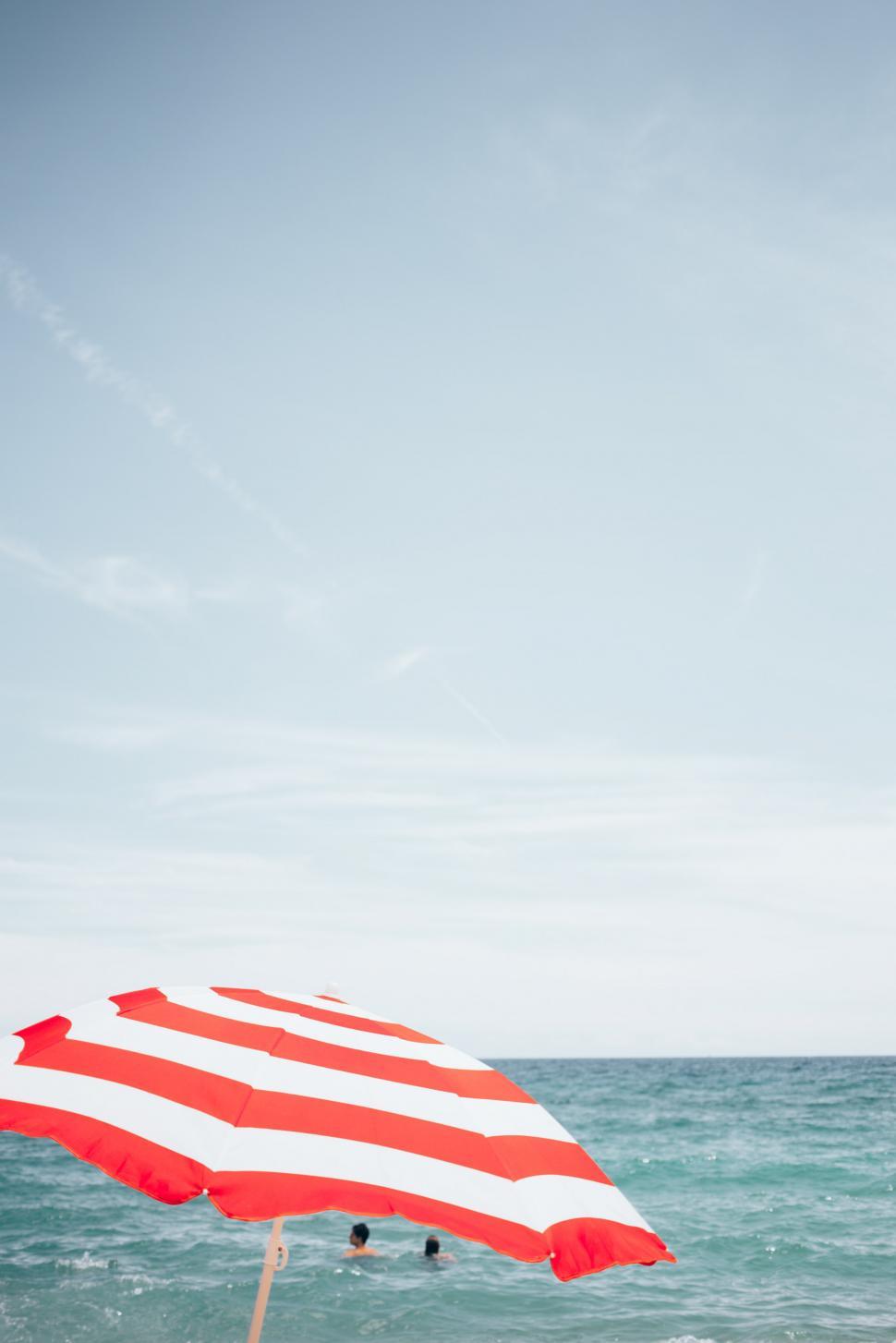 Free Image of A beach umbrella and people swimming 