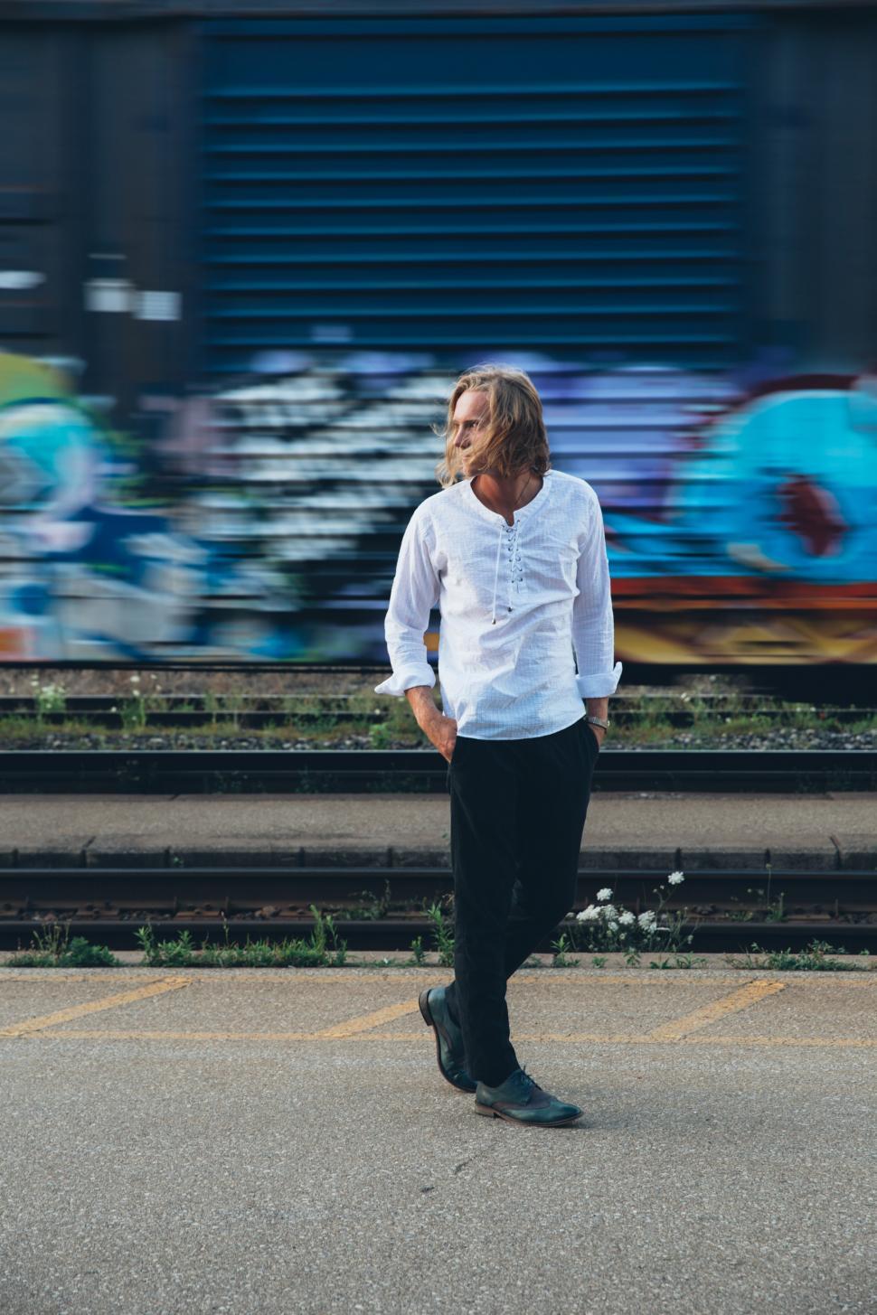 Free Image of A fashionable man walks by train tracks 