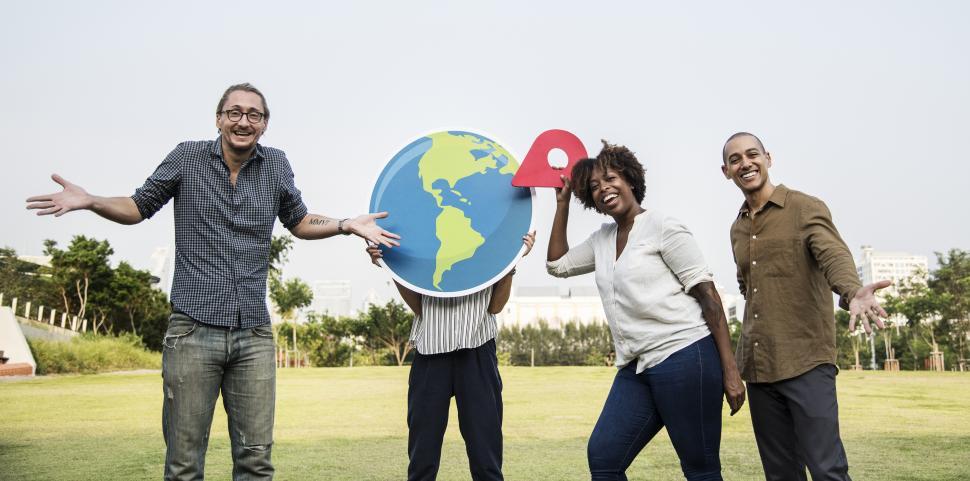 Free Image of A group of multiethnicity colleagues posing with a globe and a location shaped cardboard cutout 