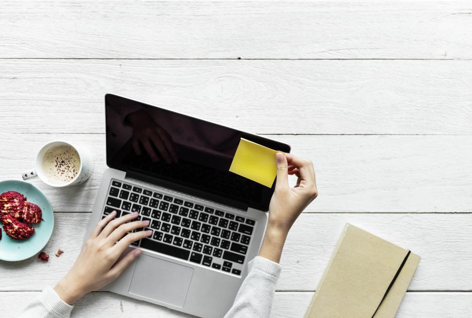 Free Image of A hand placing a sticky note on the edge of the laptop screen 