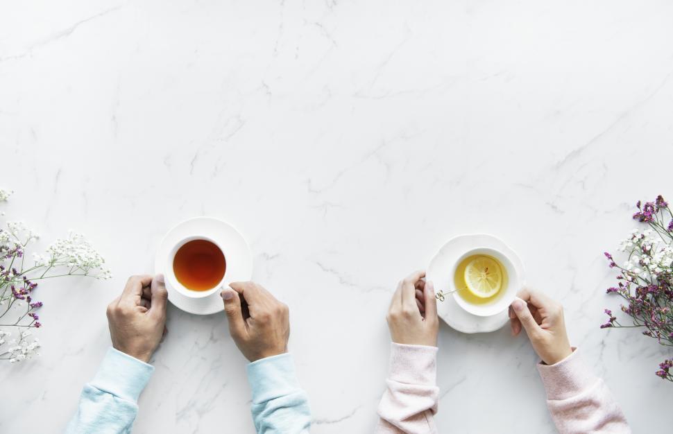 Free Image of Overhead view of hands holding cups of tea on white 