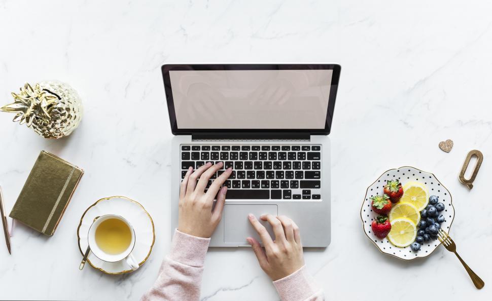 Free Image of Hands on a laptop on white marble surface with fruit and coffee 