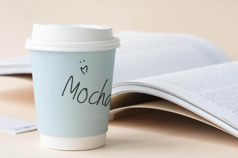 Free Image of Close up of a paper coffee cup with an open book in the background 