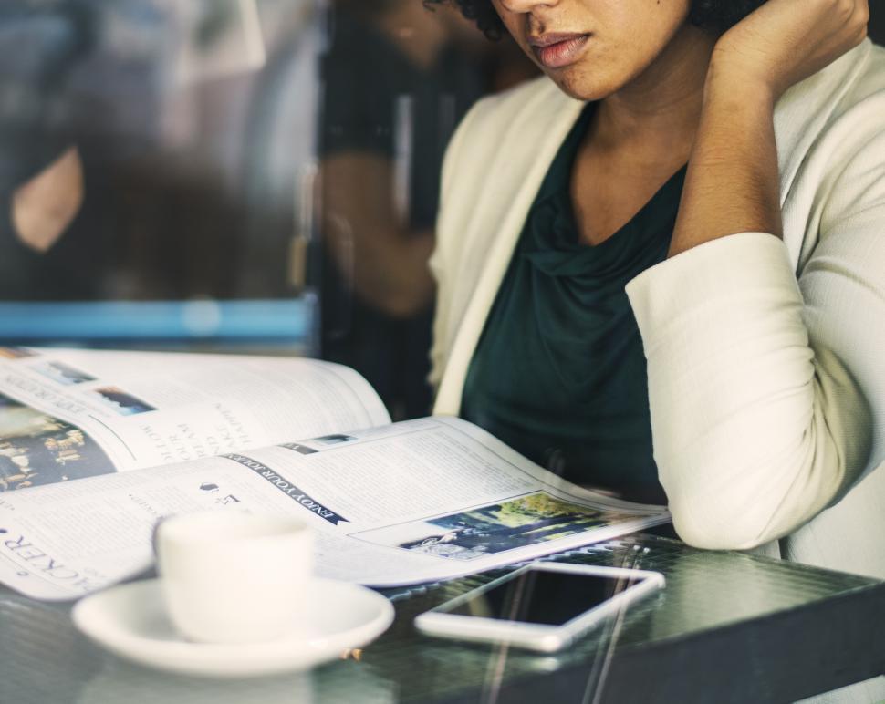 Free Image of A young African ethnicity woman reading magazine at a cafe 