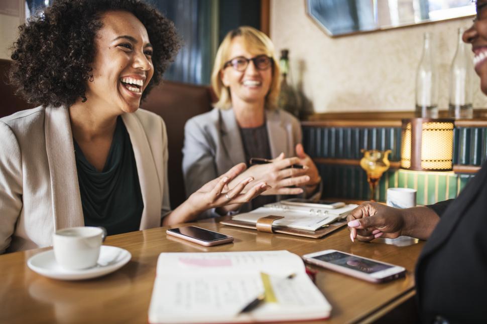 Free Image of Smiling and laughing woman coworkers seated at a cafe 