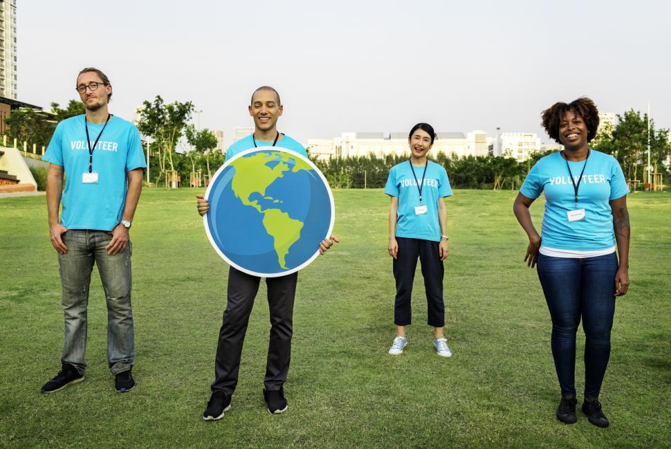 Free Image of A group of multiethnic volunteers posing with a globe in a grass field 