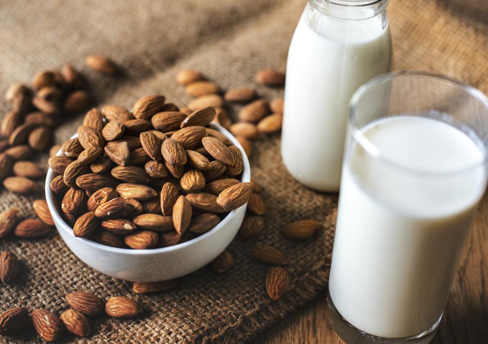 Free Photo  Milk carafe with bowl of almonds and bottle of milk high angle  view on a white wooden and piece of sack background