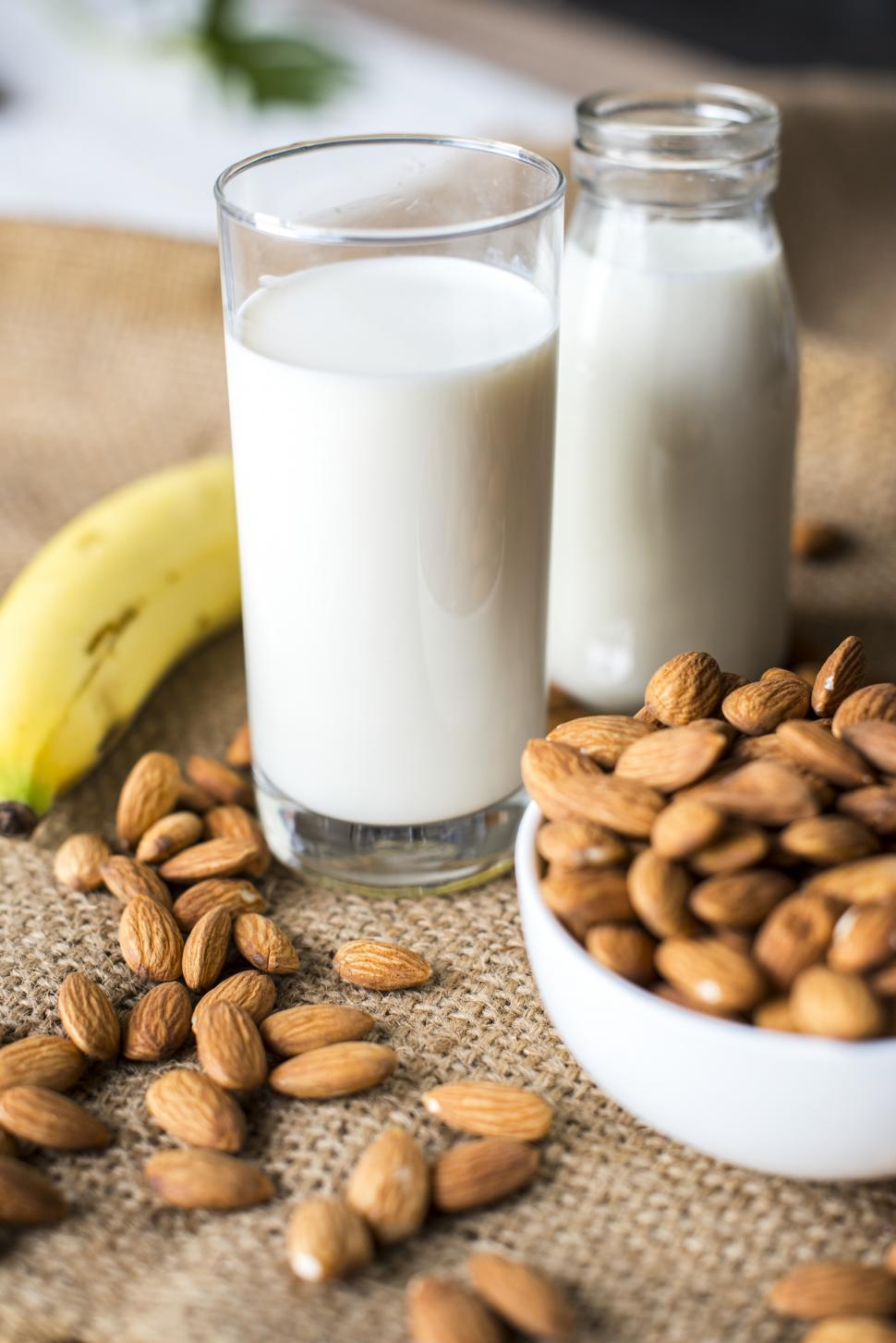 Free Photo  Milk carafe with bowl of almonds and bottle of milk high angle  view on a white wooden and piece of sack background