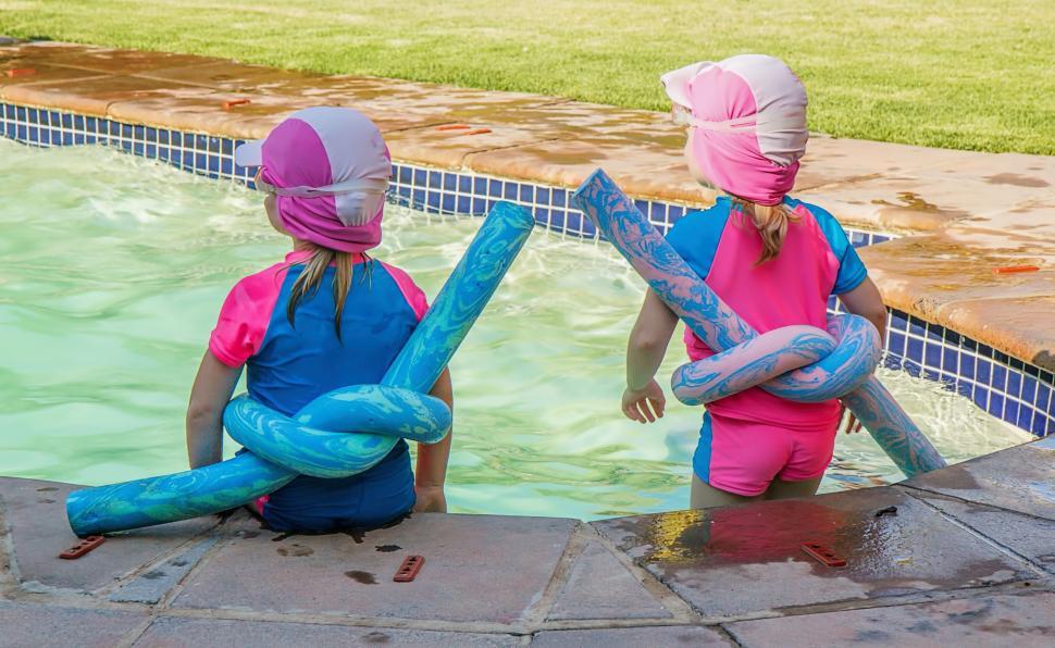 Free Image of Two Young Girls Sitting on the Edge of a Swimming Pool 