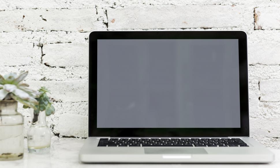 Free Image of A laptop with blank screen alongside glass flower pots the table 