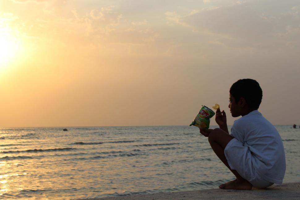 Free Image of Little Boy sitting near ocean  
