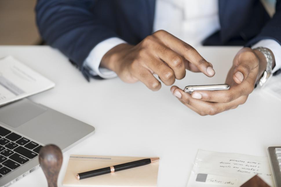 Free Image of Close up of hands holding a mobile phone over desk 