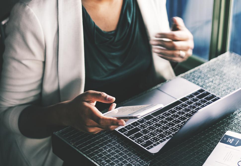 Free Image of A young woman holding her mobile phone over a laptop at a cafe 