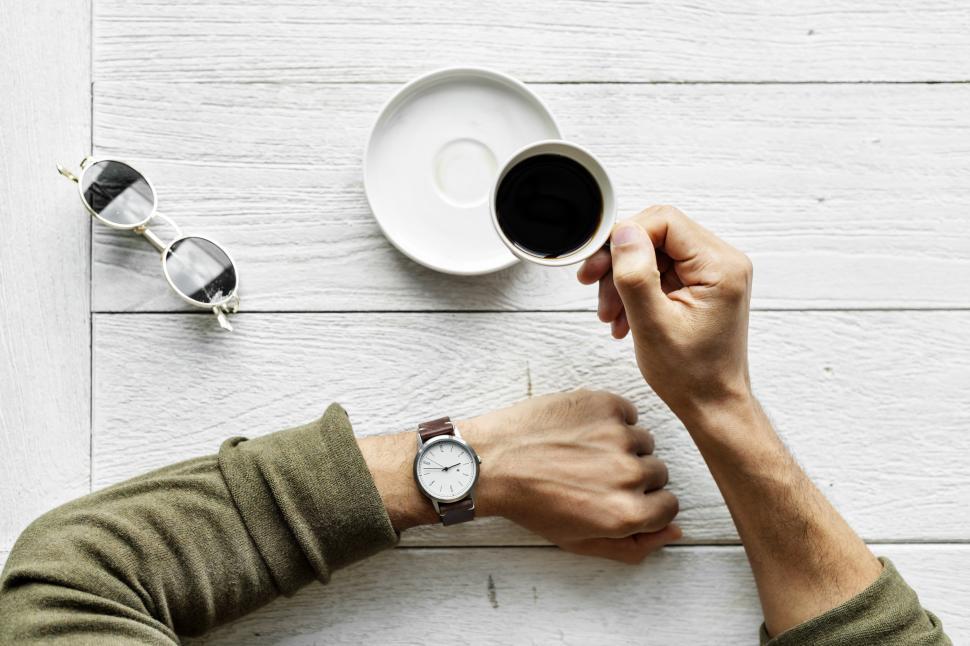 Free Image of Overhead view of a hand holding a cup of coffee, checking watch for time 