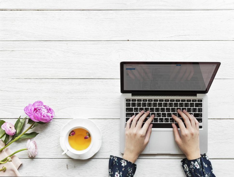 Free Image of Overhead view of hands typing on the laptop with flowers and tea 