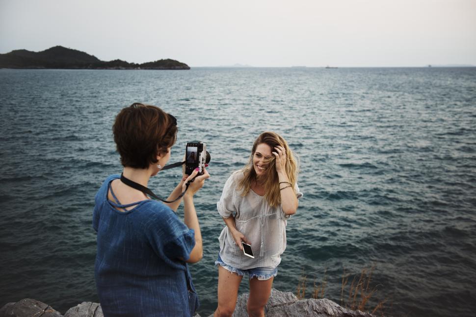 Two young women taking photographs at a rocky seashore