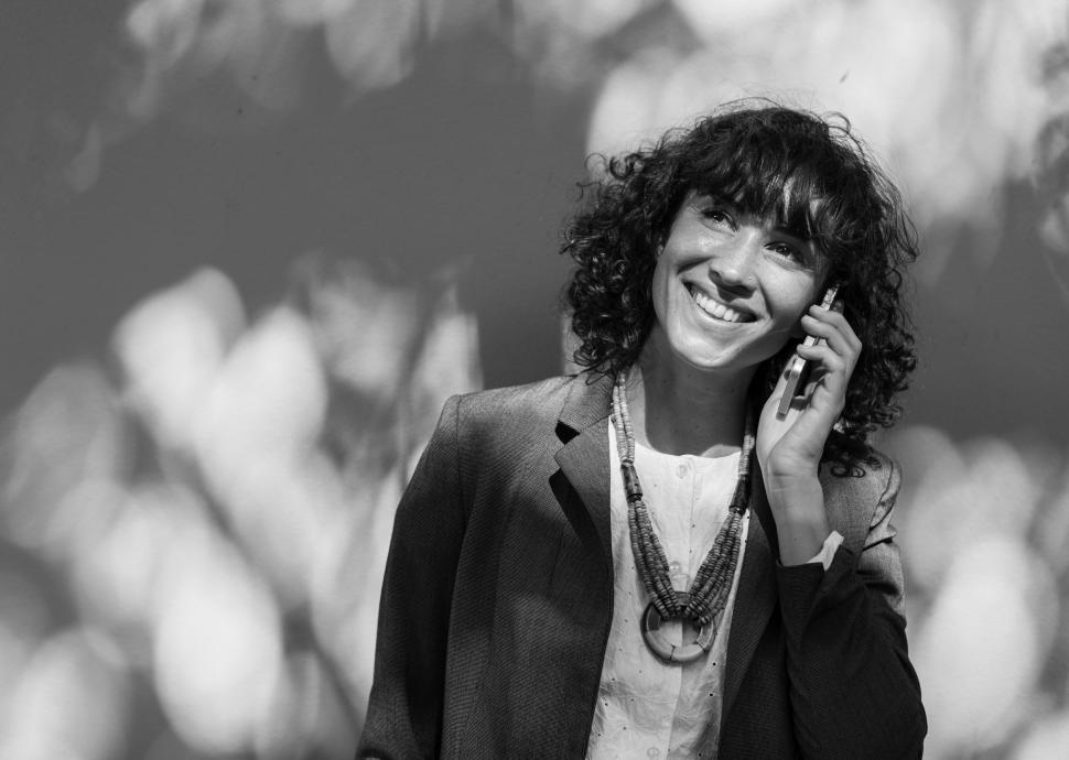 Free Image of Black and white photo of a smiling young woman listening to a call on her mobile phone 