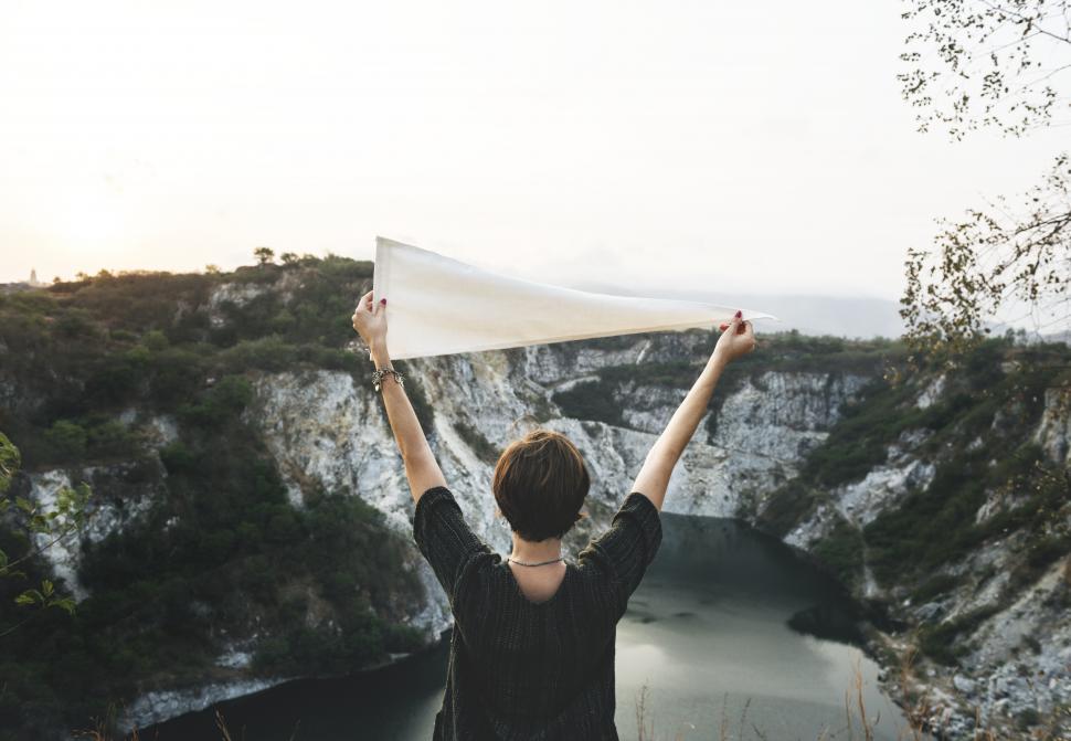 Free Image of A young female hiker holding a white flag high above a lake 