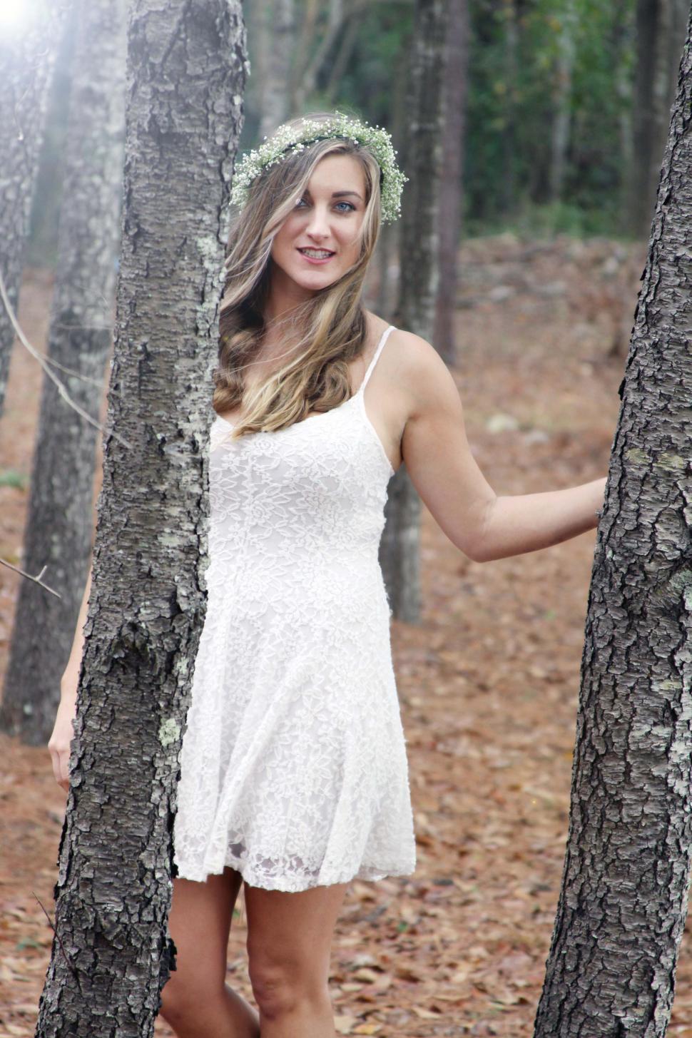 Free Image of Woman with floral wreath smiling and posing with trees 