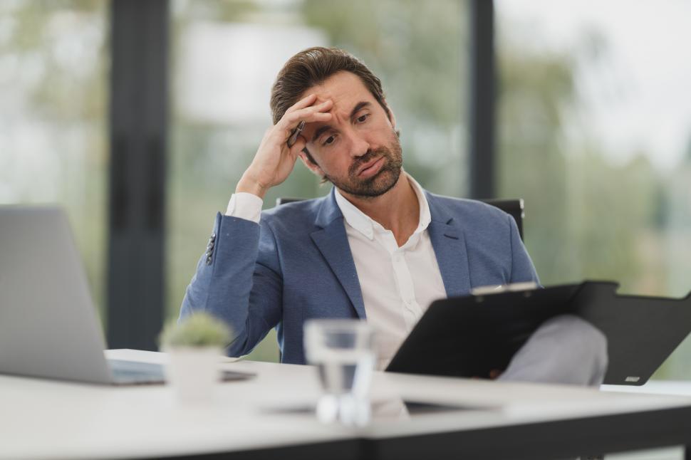 Free Image of Pensive young man with documents and laptop in office 